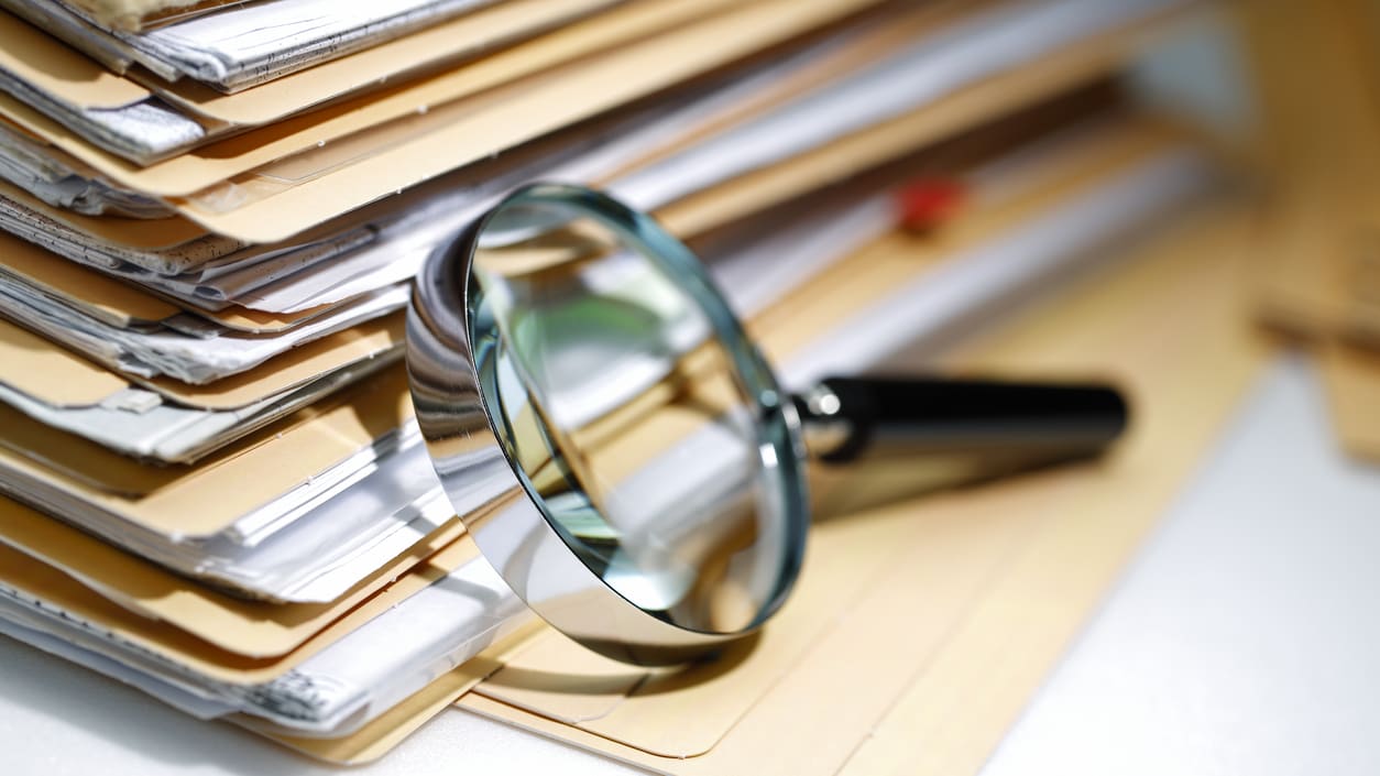 A magnifying glass on a stack of folders full of paper documents